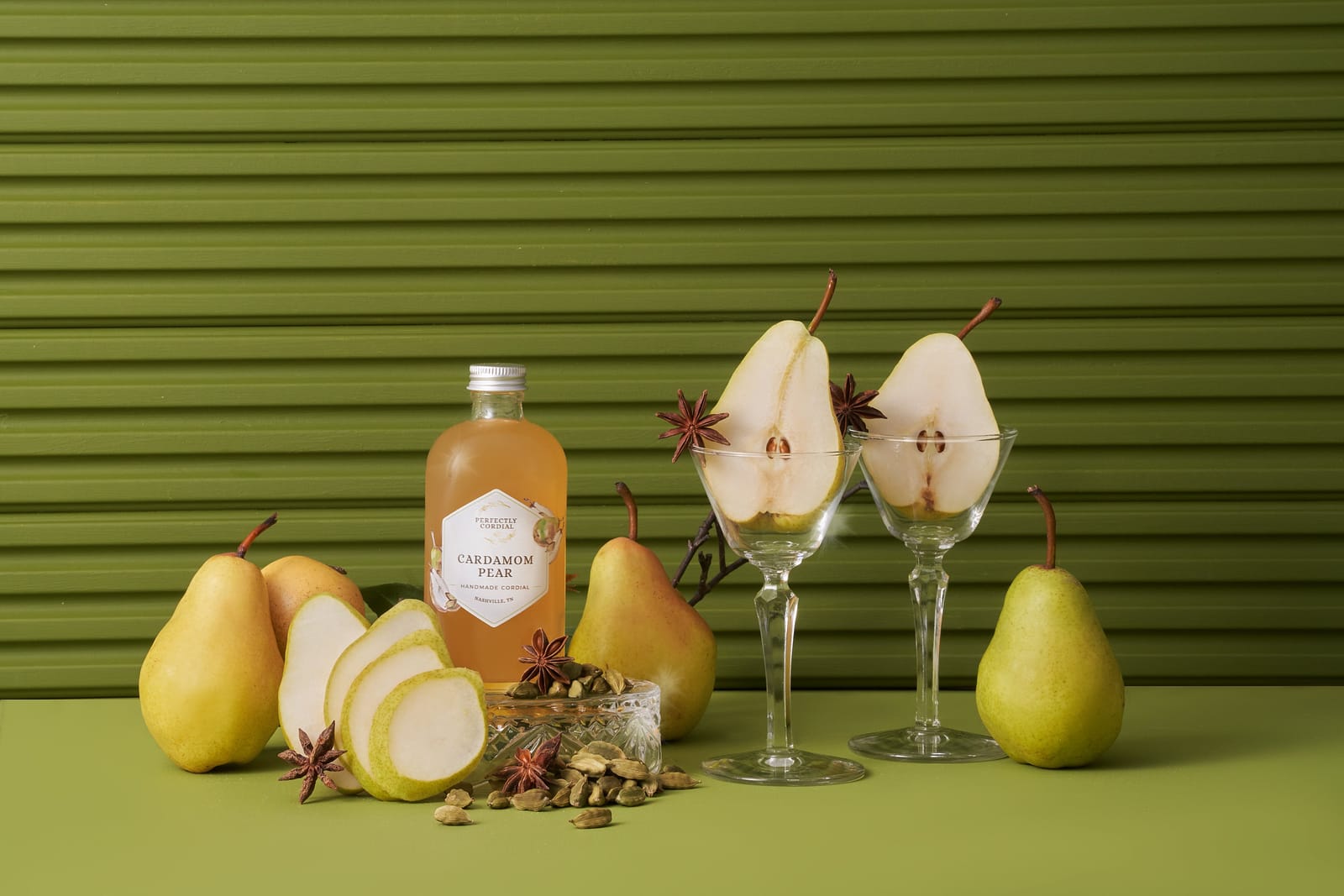 Cardamom Pear cordial with fresh pears, star anise and cardamom pods against an olive green wall