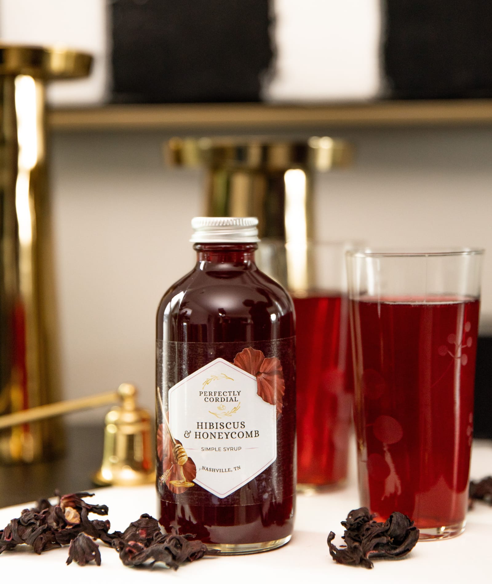 Hibiscus and Honeycomb bottle with two glasses of deep red hibiscus cooler and dried hibiscus flowers